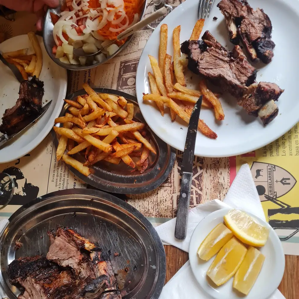 An asado lunch seen from above: grilled meat, fries and lemon