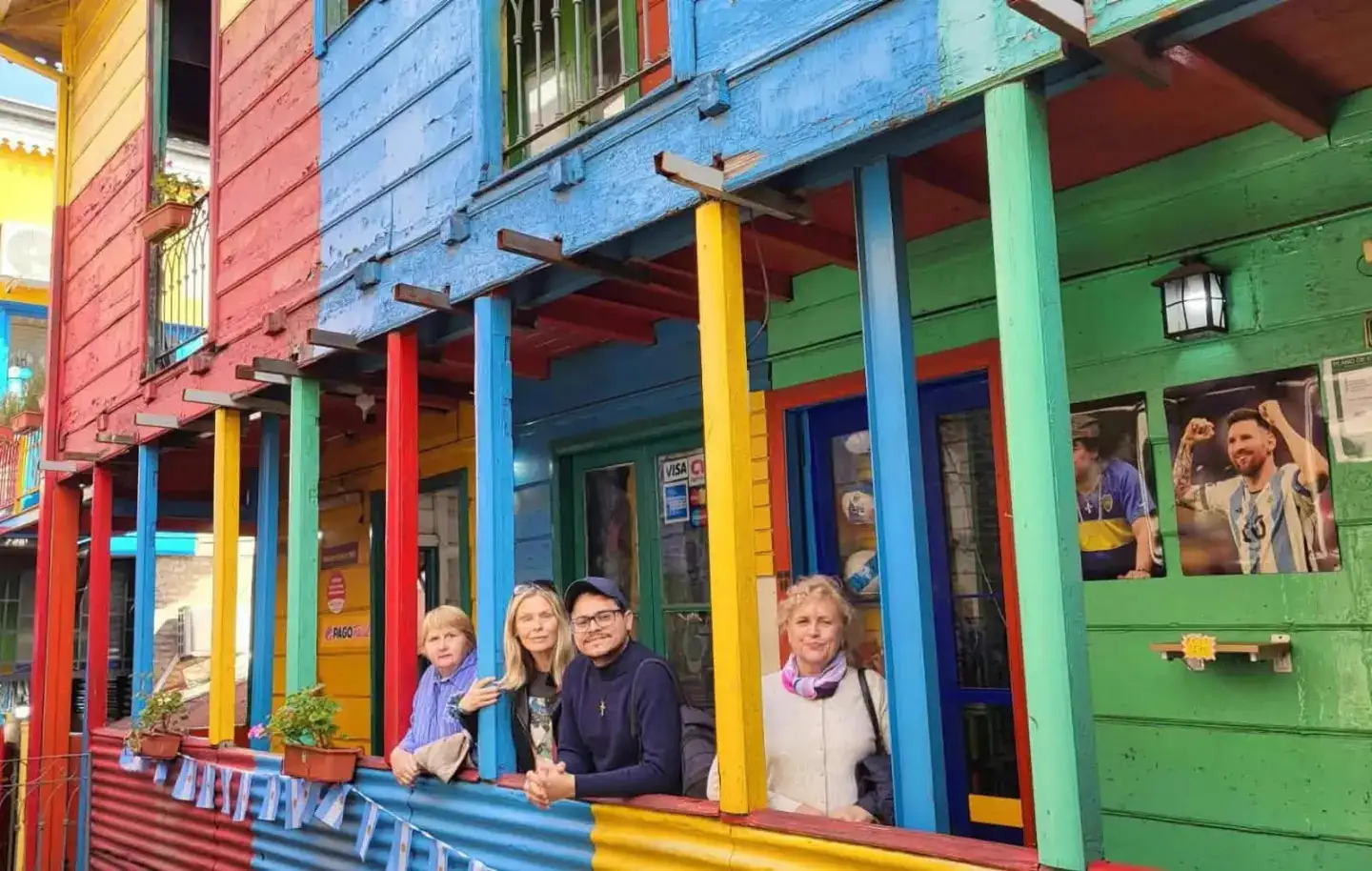 Sebastián and three guests leaning on the balcony of a painted house in Caminito